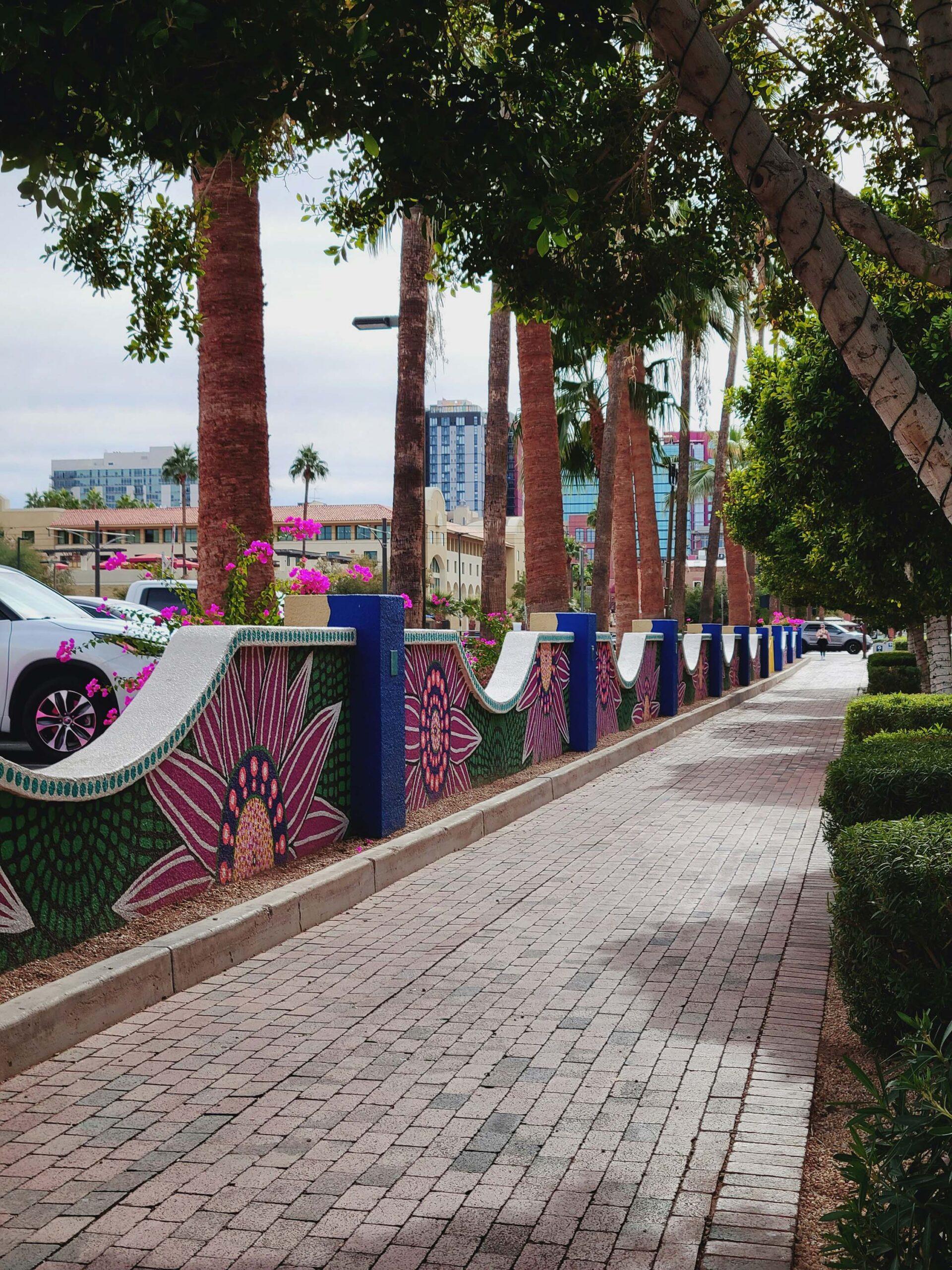 A palm tree-lined brick walkway bordered with low walls covered in mosaic tiles.